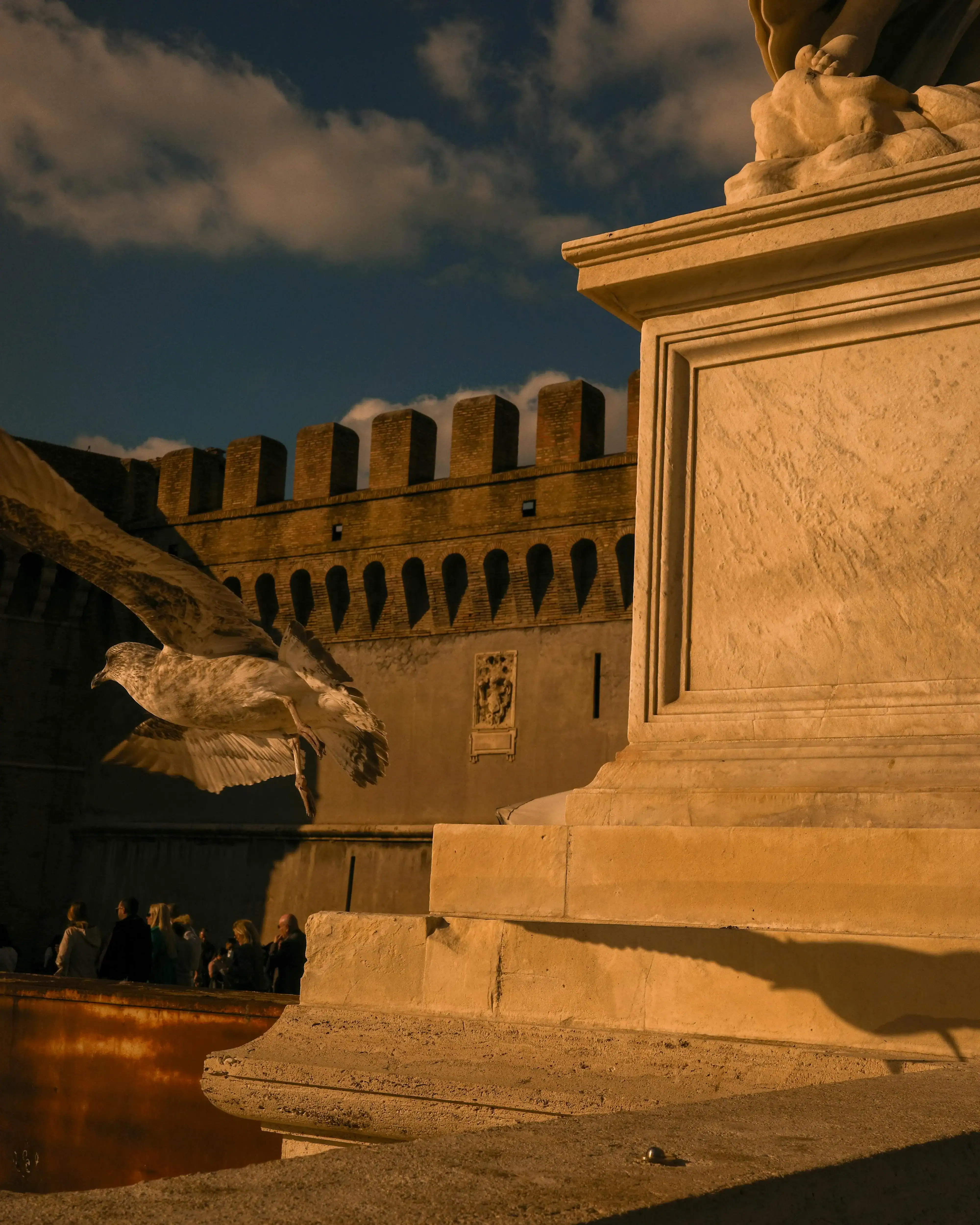 Festungsmauer der Engelsburg in goldenem Abendlicht mit Zinnen und Engelsstatue im Vordergrund