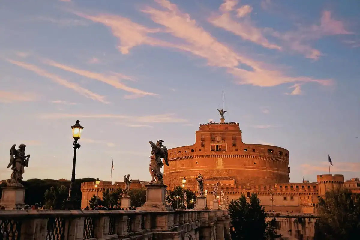 Engelsburg in Rom bei Sonnenuntergang mit pinkfarbenem Himmel und Ponte Sant'Angelo im Vordergrund